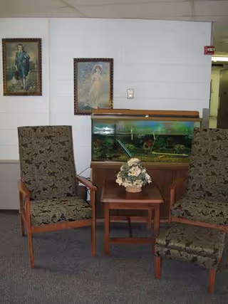 Two upholstered chairs flank a fish tank on a wooden table in a lounge.