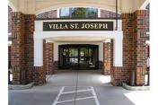 Entrance to Villa St. Joseph building with a covered walkway supported by brick columns and a sign above the entrance reading 'VILLA ST. JOSEPH'.