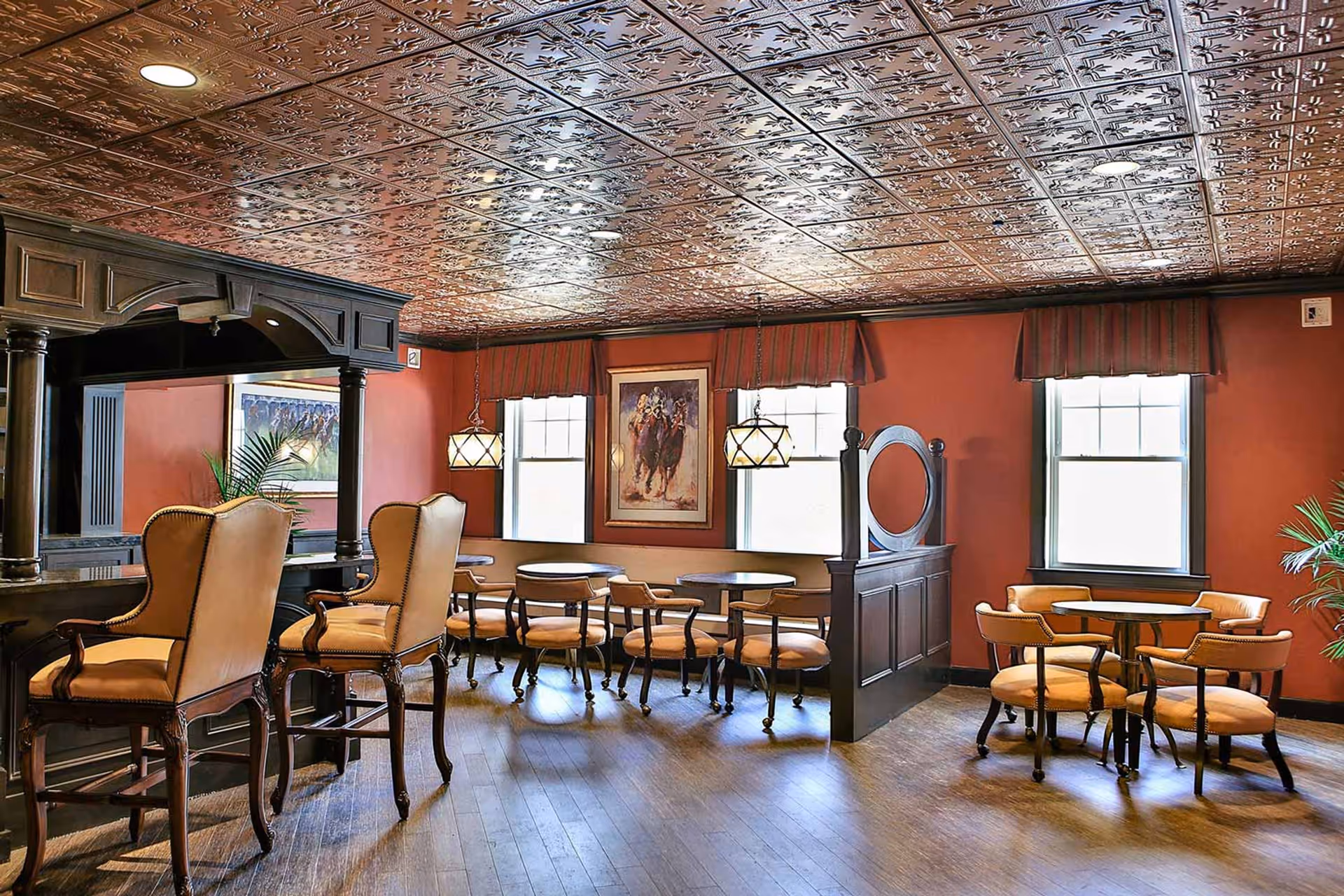 Cozy dining/lounge area with a wooden bar, round tables and upholstered chairs beneath a decorative tin ceiling.