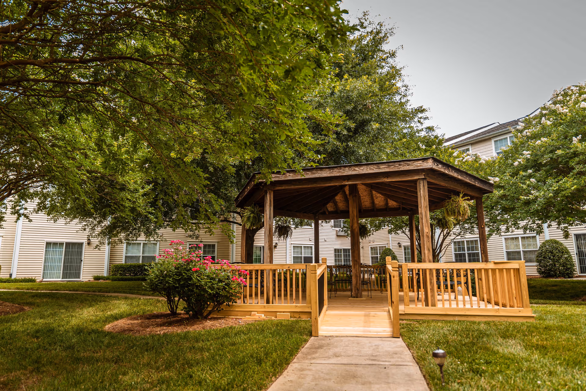A wooden gazebo on a raised deck in a landscaped courtyard surrounded by apartment windows and trees.