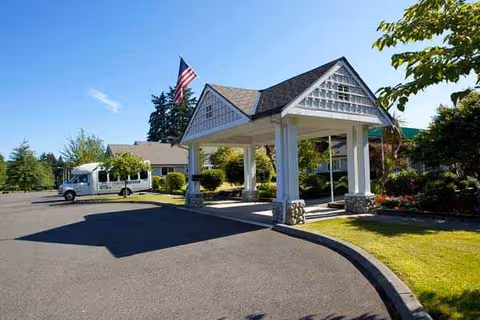 Senior living facility entrance with covered drop-off, flag, and landscaped surroundings.