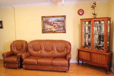 Yellow-walled living room with brown leather sofa and glass-front cabinet.