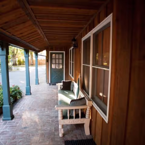 Wooden exterior porch with a bench, brick floor, and turquoise columns.