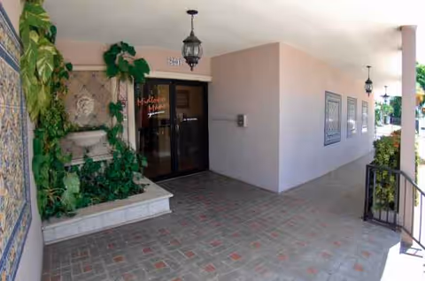 Exterior entrance to Midtown Manor with glass doors, tiled walkway, and greenery.