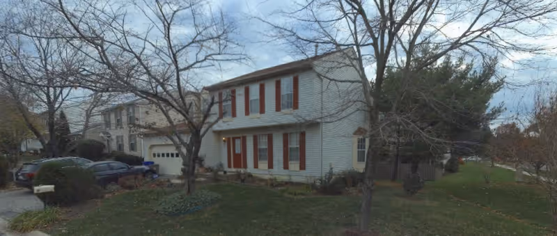 Two-story residential building with white siding and red shutters, surrounded by leafless trees and a grassy lawn. Several cars are parked in the driveway and along the street.