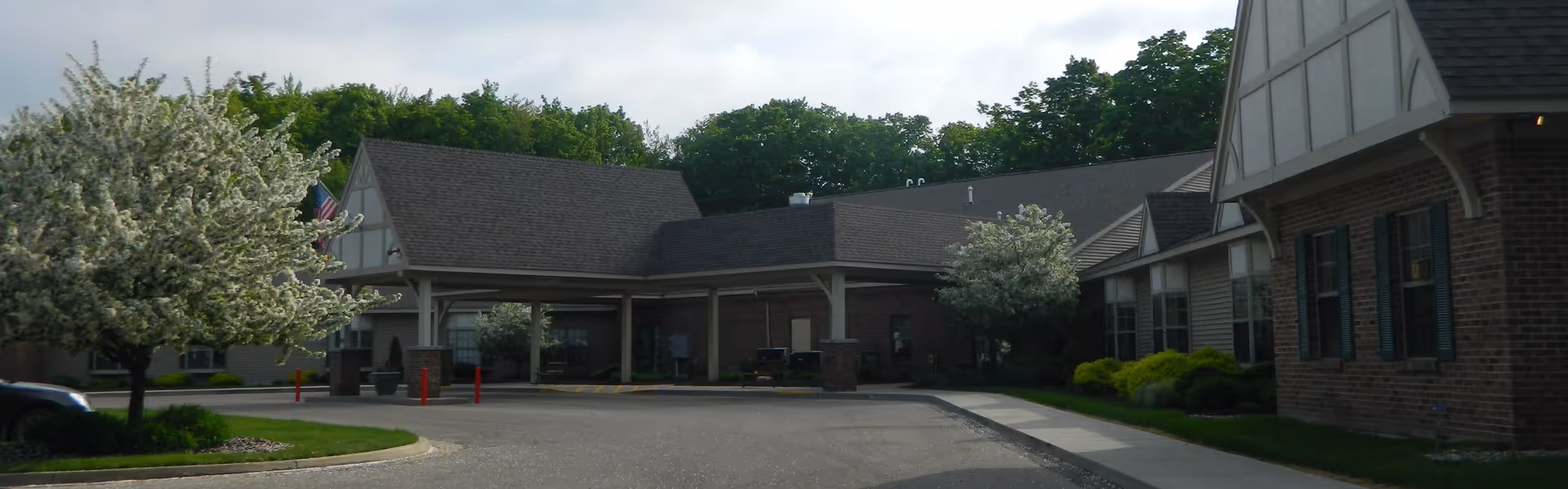 Exterior view of a senior living facility named Aspen Ridge featuring a covered entrance, brick and siding walls, flowering trees, and a paved driveway.