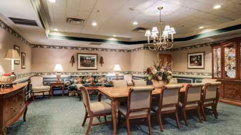 Elegant dining room with a long table, chairs, chandeliers, and a floral centerpiece.