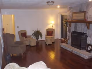 Cozy living room with hardwood floors, a stone fireplace, three armchairs, a floor lamp and a small plant.