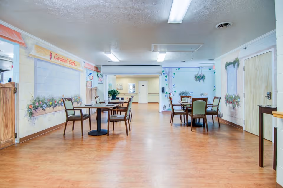 Dining area with several tables and chairs on a wood floor and muraled walls including a 'Cardinal Cafe' sign.