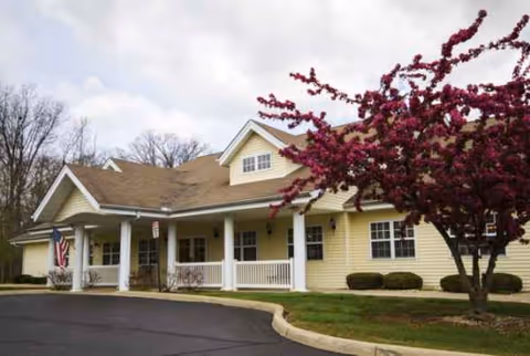 Yellow senior living facility with a covered front porch and blooming purple tree.