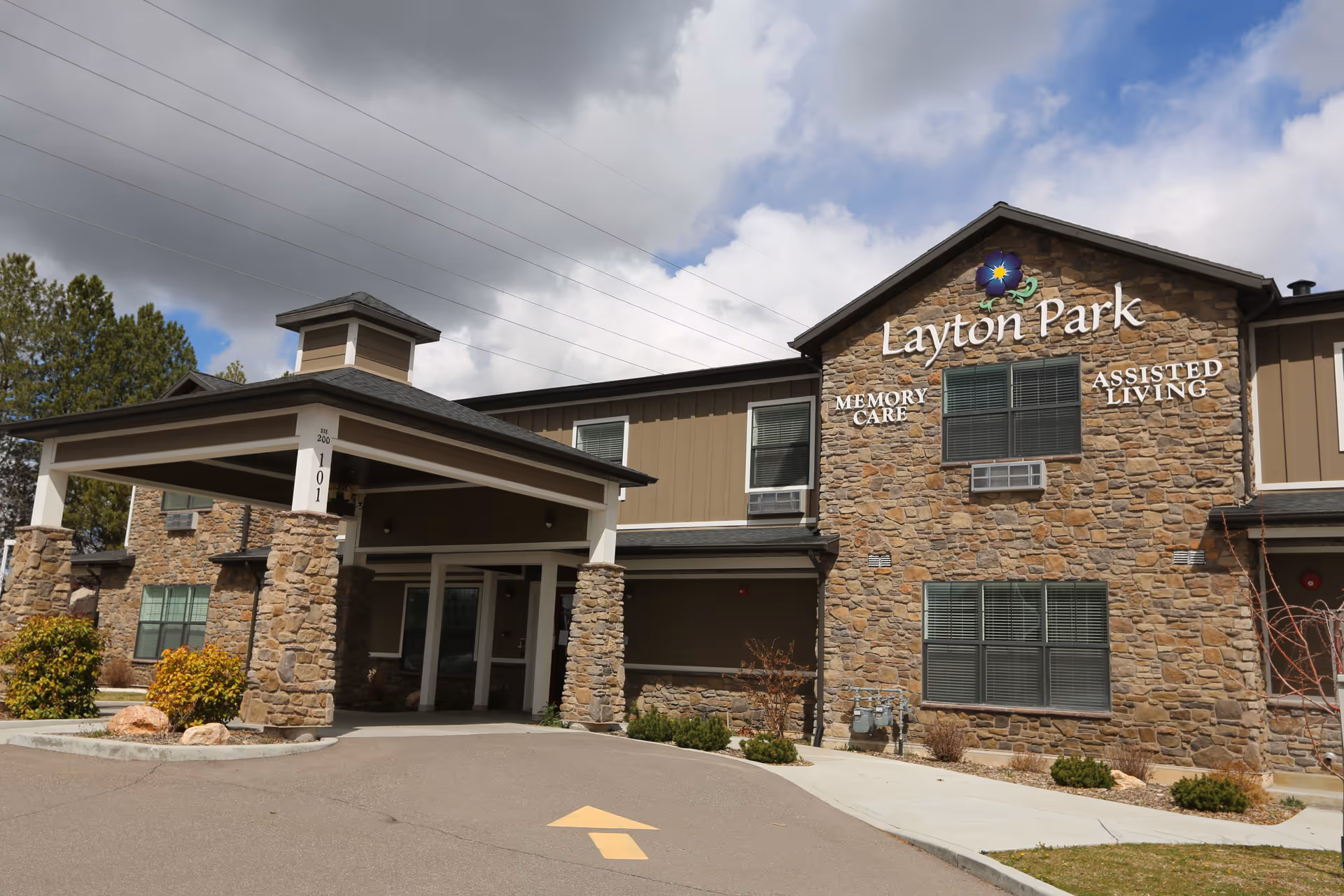 Front entrance of the Layton Park Memory Care assisted living building with stone facade, covered porte-cochère, and visible signage.