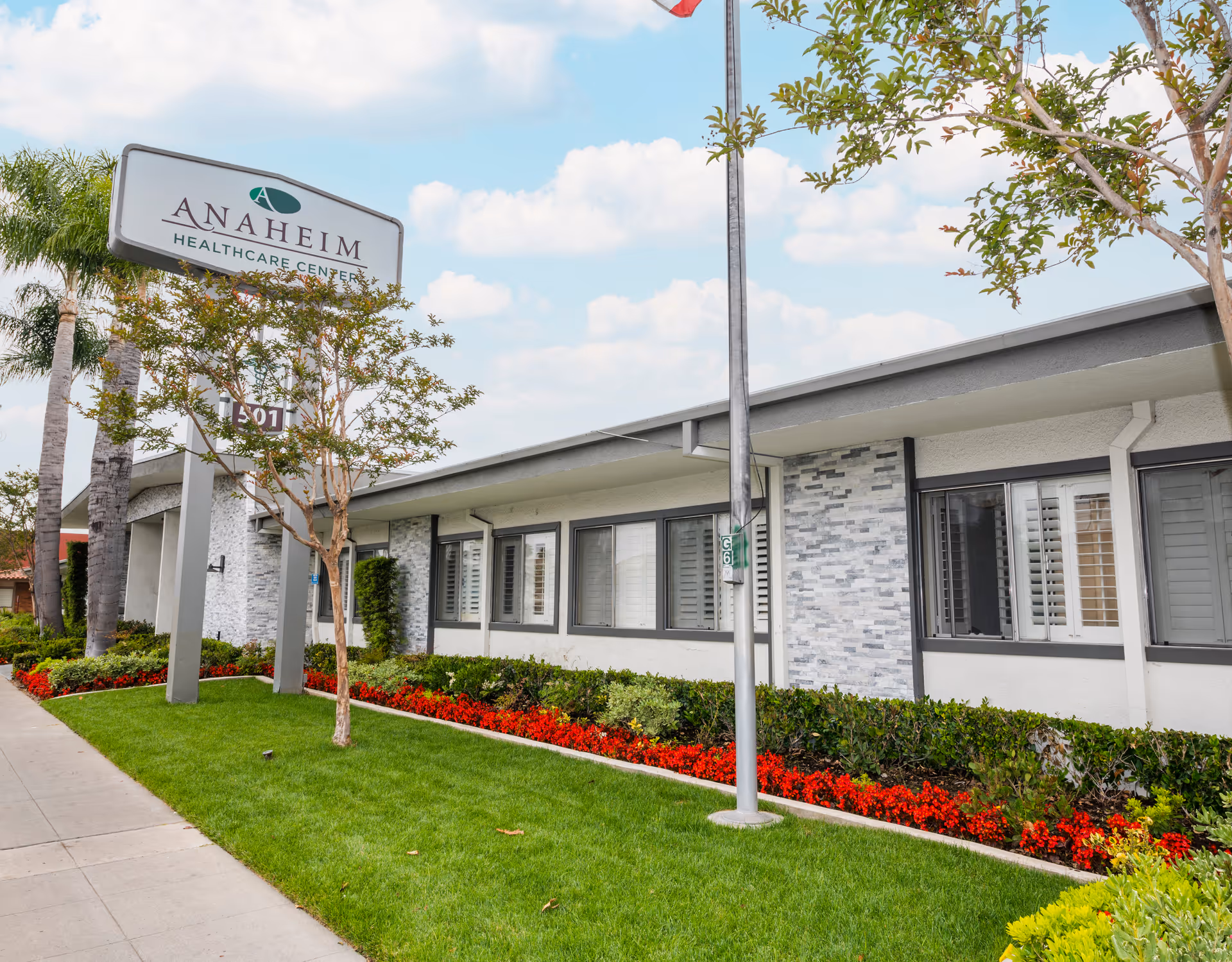 Front exterior of the Anaheim Healthcare Center building with its sign, landscaped lawn, and flower beds.