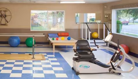 Rehabilitation exercise room with stationary bike, balance apparatus, and therapy balls in a bright facility.