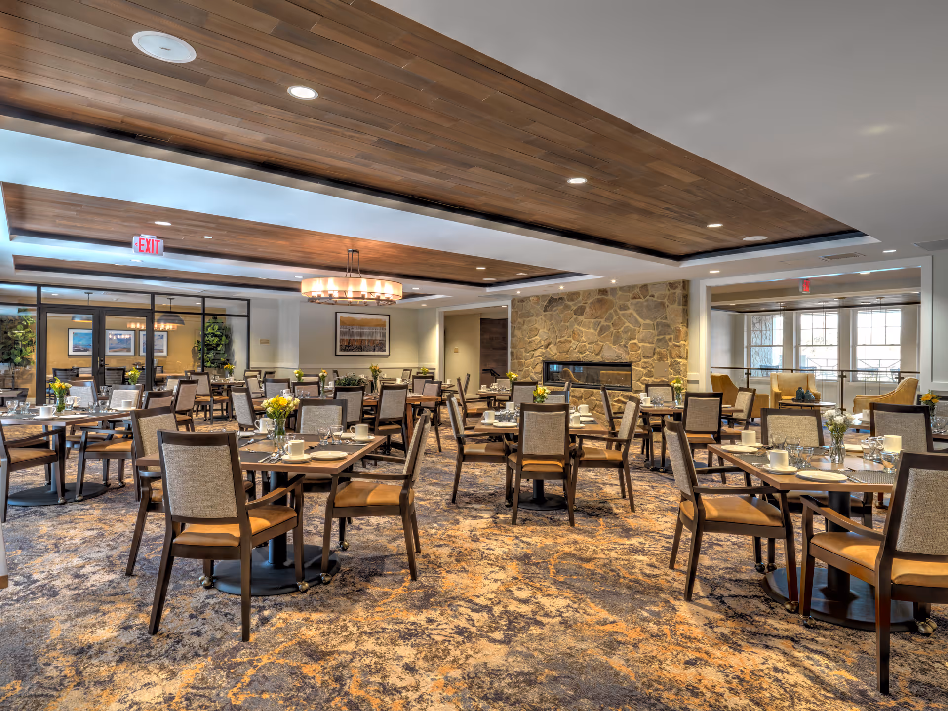 Spacious dining room with multiple set tables and chairs, a wood-accent ceiling, and a stone accent wall.