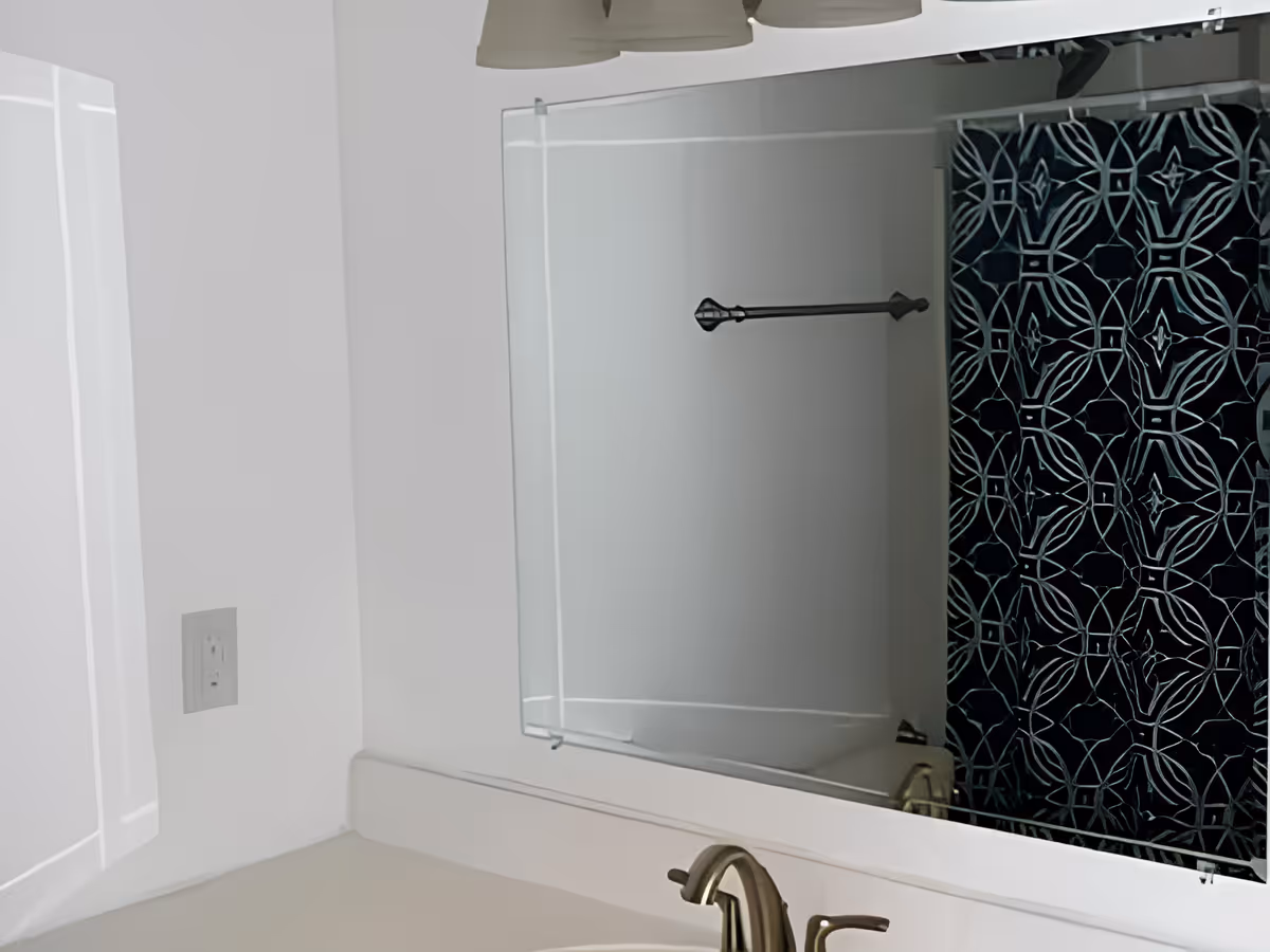 A bathroom interior featuring a white countertop with a silver faucet, a large mirror above the sink, a towel bar mounted on the wall, and a shower area with a dark blue and white patterned shower curtain.