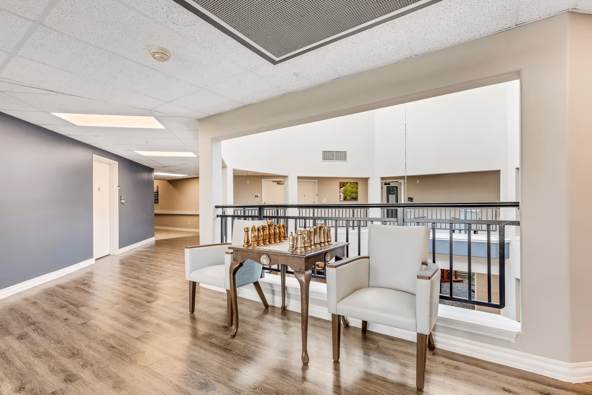 Atrium-level interior hallway with two armchairs and a small table holding a chess set overlooking the open atrium.