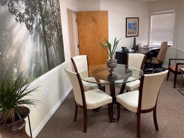 Dining room at Cloudberry Lodge with round glass table, cream chairs, and potted plants.