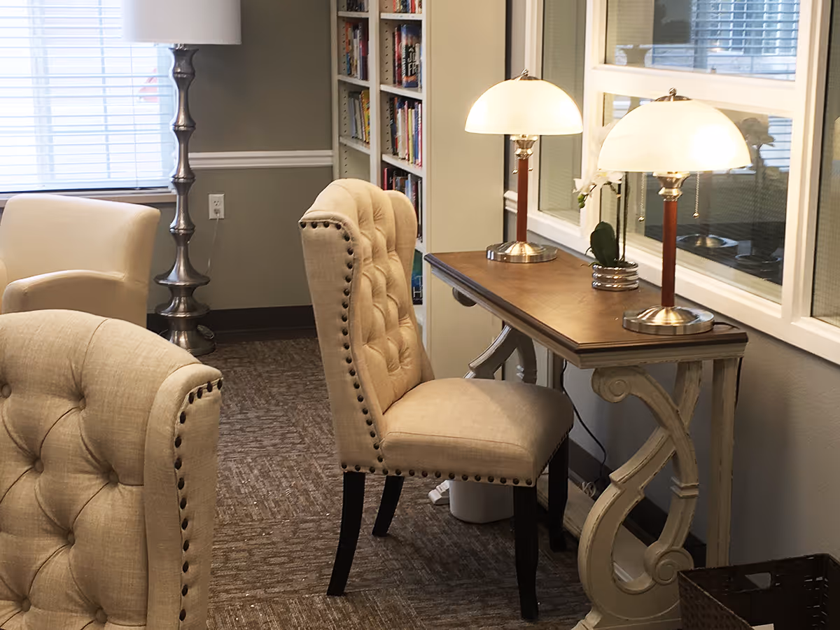 Upholstered tufted chairs around a wooden console table with two lamps in a cozy interior sitting area.