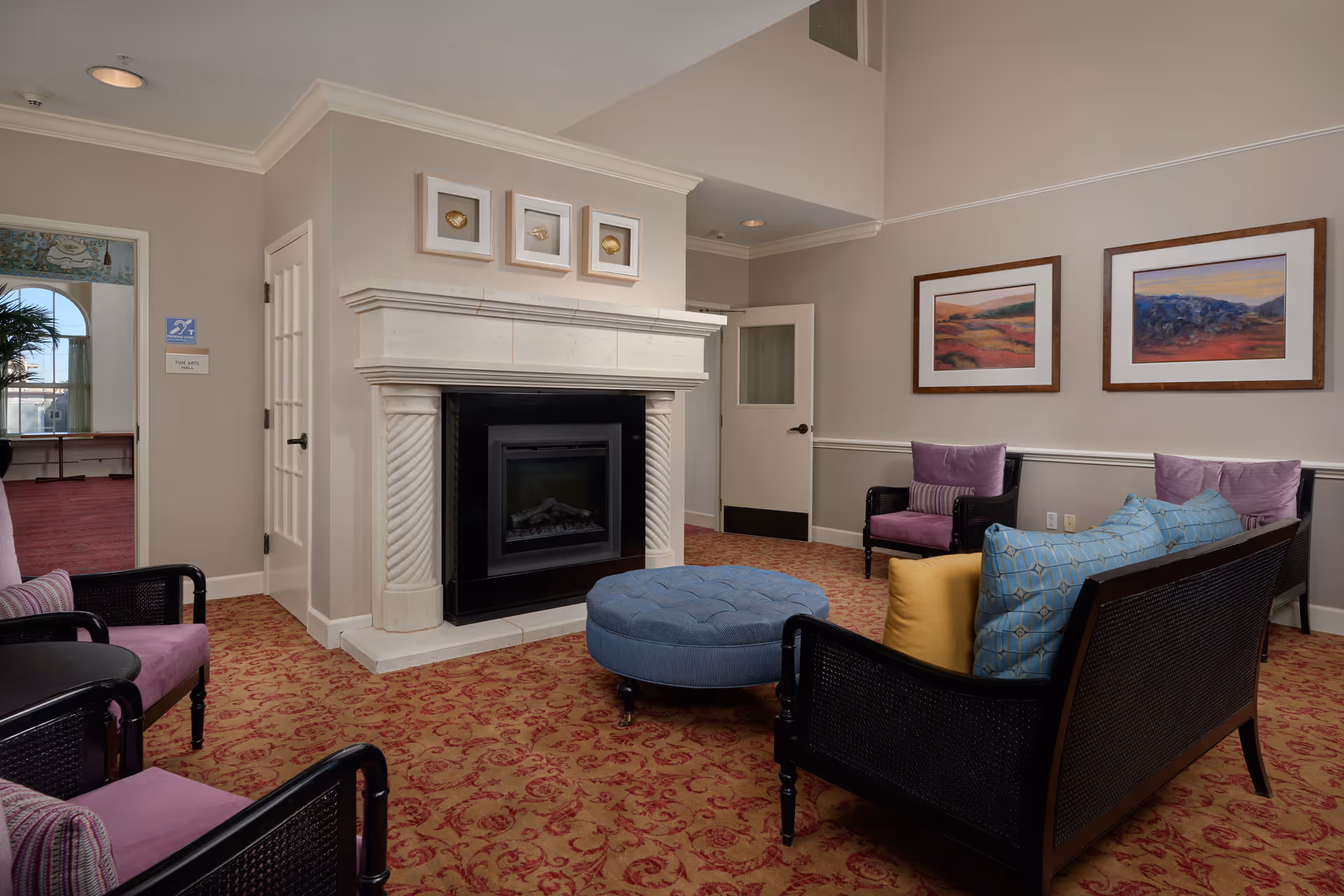 Cozy common room with a stone fireplace, upholstered chairs, sofa, ottoman, and framed artwork on the walls.