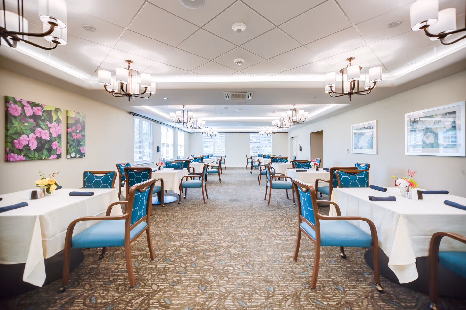 Bright, spacious dining room with multiple tables set with white tablecloths and teal-upholstered chairs.