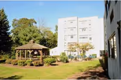 A multi-story white senior living building with a grassy courtyard and gazebo.