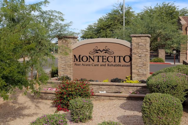 Stone sign for Montecito Post Acute Care and Rehabilitation surrounded by landscaped bushes and trees with a clear blue sky in the background.
