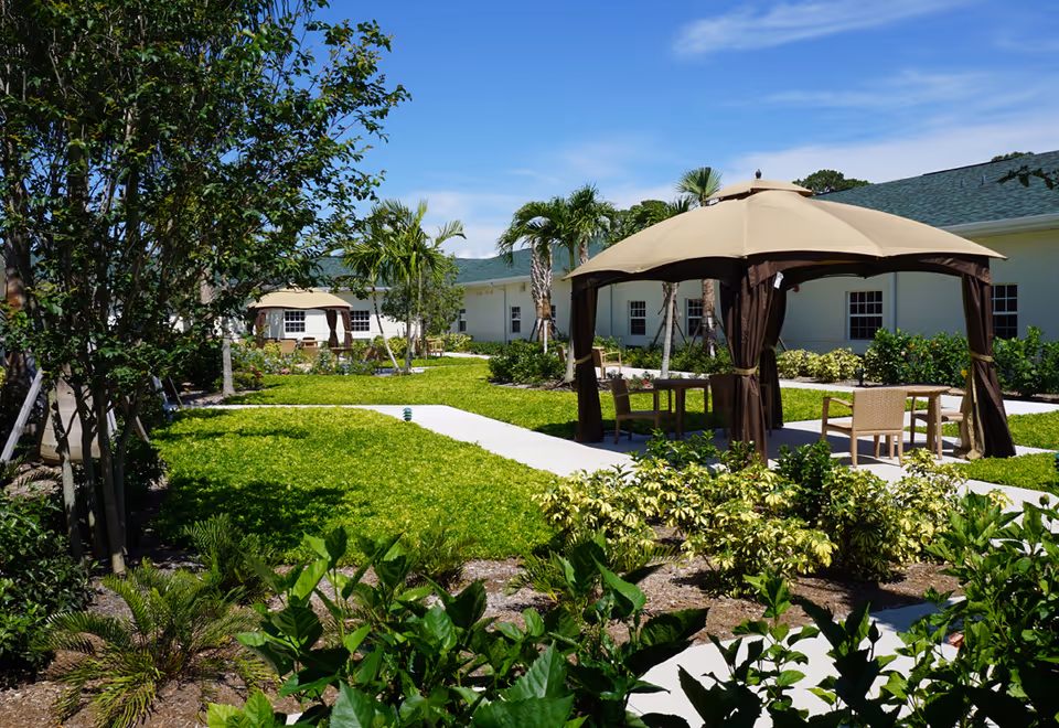 Well-maintained courtyard with canopy seating, walkways, palm trees and surrounding single-story buildings under a blue sky.