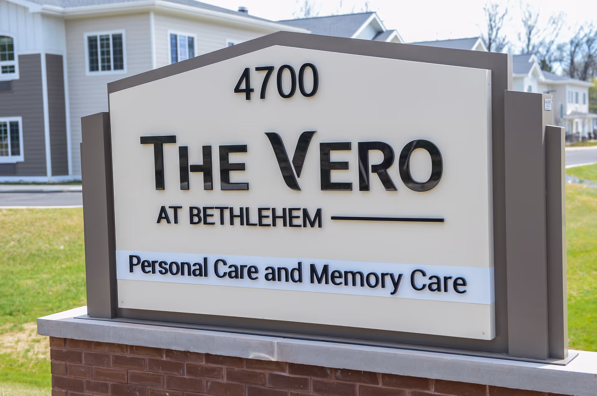 Outdoor sign for The Vero at Bethlehem, a personal care and memory care facility, with the address number 4700 displayed above the name. The sign is mounted on a brick base with a residential building visible in the background.
