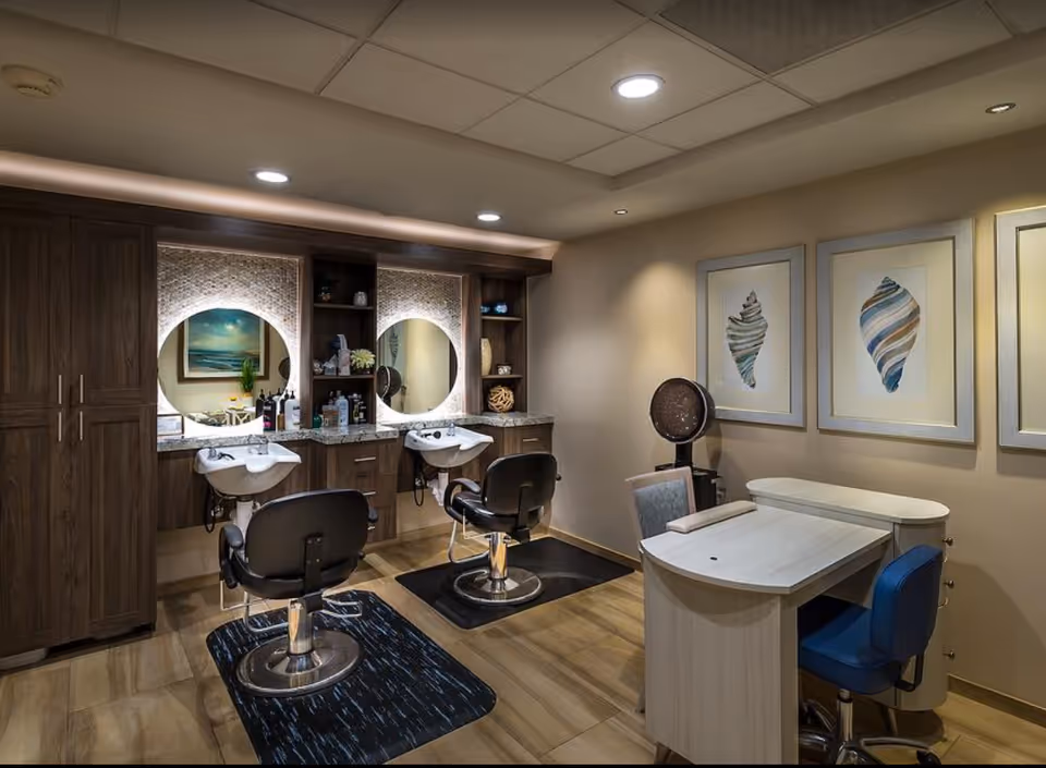 Interior salon area with two styling chairs and wash sinks in front of round mirrors, cabinetry, and a manicure table with chairs.