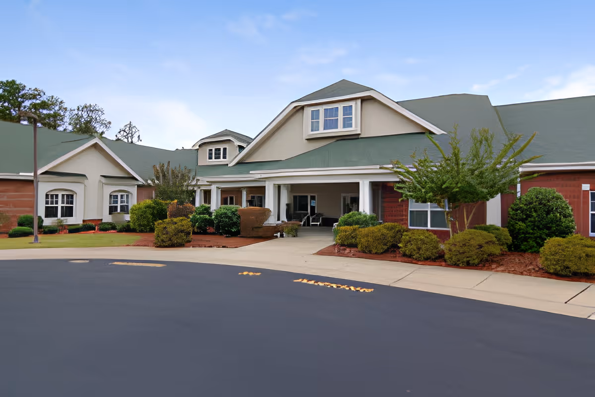 Front exterior of a single-story care facility with a covered entrance, green roofs, and landscaped shrubs.