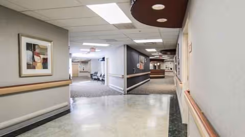Interior hallway of a senior living facility with artwork, seating areas, and handrails along walls.