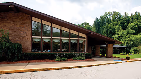 Low single-story brick healthcare building with large slanted windows, a covered entrance, and landscaped grounds.