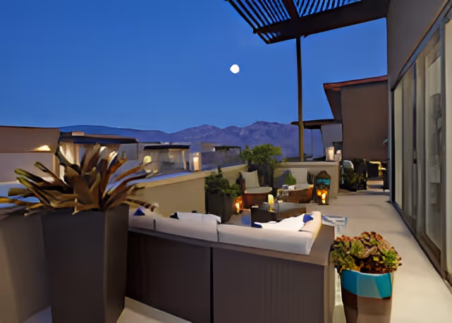 Rooftop terrace with outdoor seating, potted plants, lanterns, and mountain views under a twilight sky.