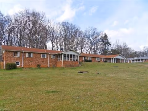 Long brick senior living facility with a grassy lawn and leafless trees.