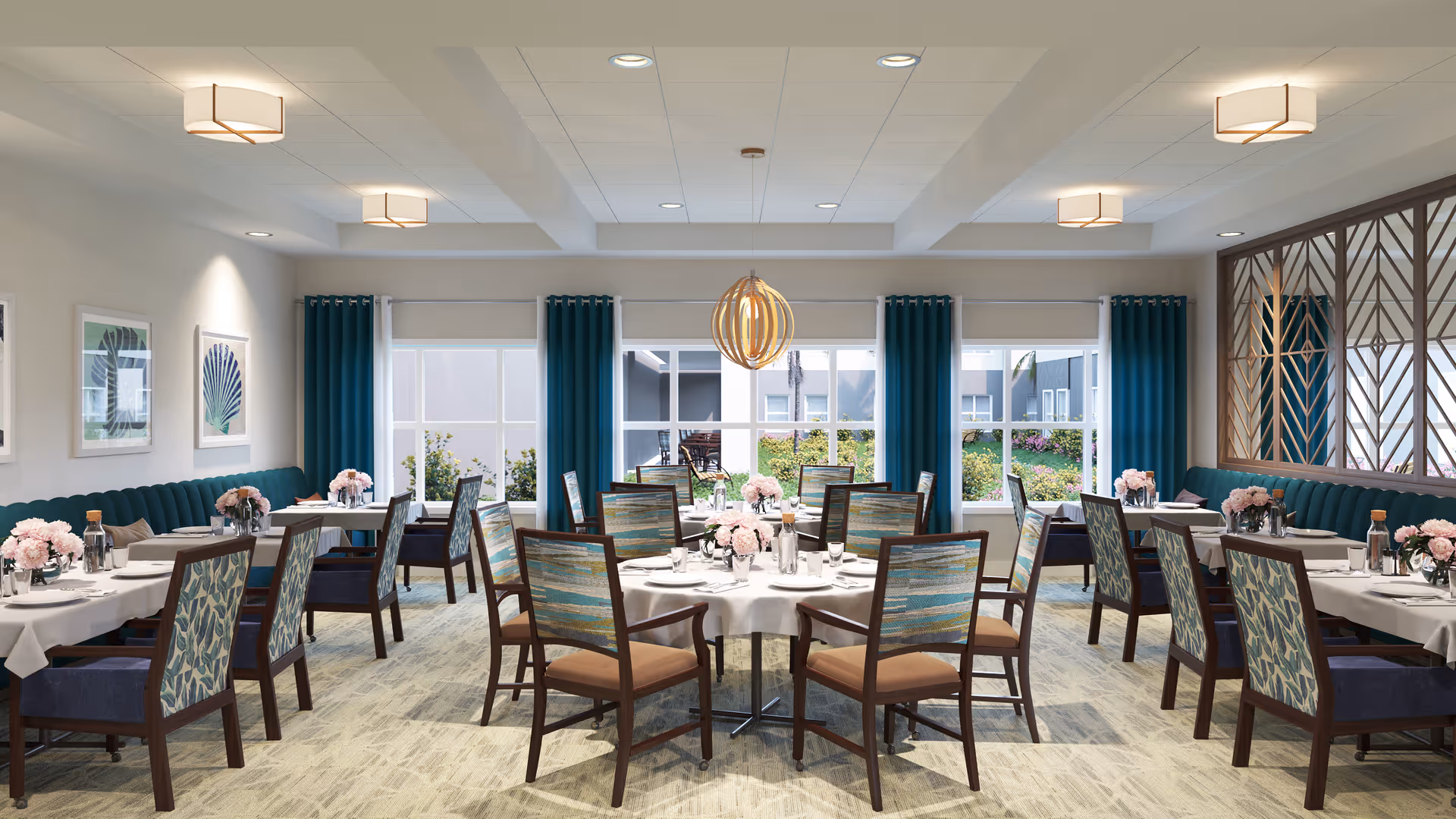 A bright and elegant dining room with round and rectangular tables covered with white tablecloths, each set with plates, glasses, and pink floral centerpieces. The room features teal curtains, patterned chairs with wooden frames, and large windows showing a garden outside. The ceiling has recessed lighting and modern light fixtures.