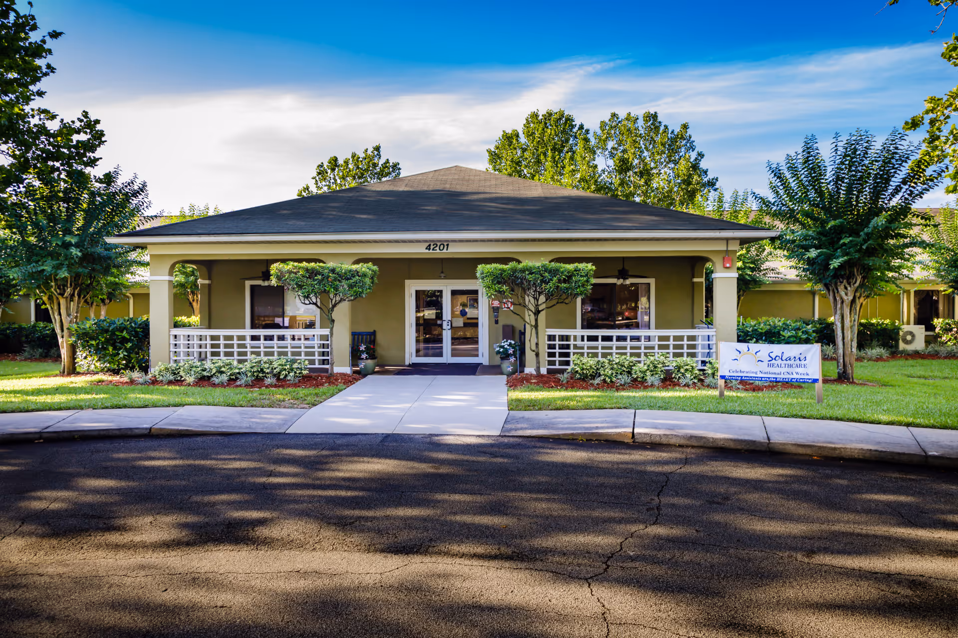 Front exterior view of Solaris HealthCare Osceola building with a paved driveway, manicured lawn, trees, and a sign on the right side near the entrance.