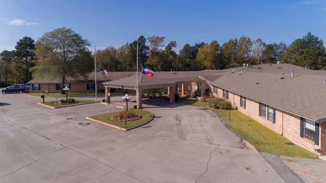 Exterior view of Southland Rehabilitation And Healthcare Center showing a single-story brick building with a covered entrance, two flagpoles with American and Texas flags, surrounding trees, and a parking area.
