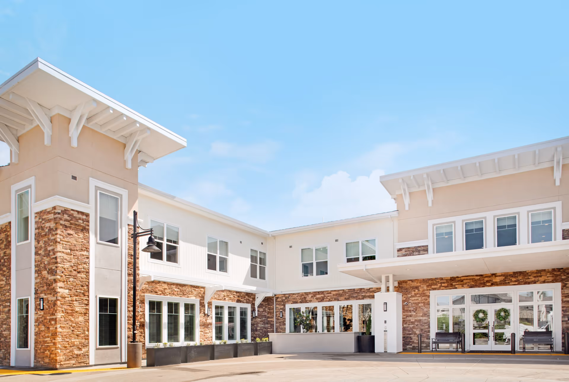Front exterior of a modern two-story senior living facility with stone accents, large windows, and a covered entrance.