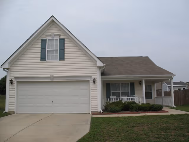 White house with a two-car garage, front porch, and green shutters.