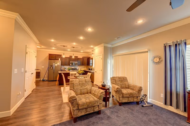 Open-plan living area with two upholstered armchairs and a side table, looking toward a kitchen and dining area.
