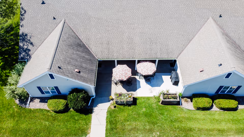 Aerial view of a senior living facility courtyard with two patio umbrellas, seating, walkways and lawns between two building wings.