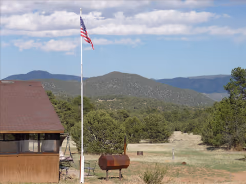 Outdoor facility area with a small building, flagpole, grill, and hills in the distance