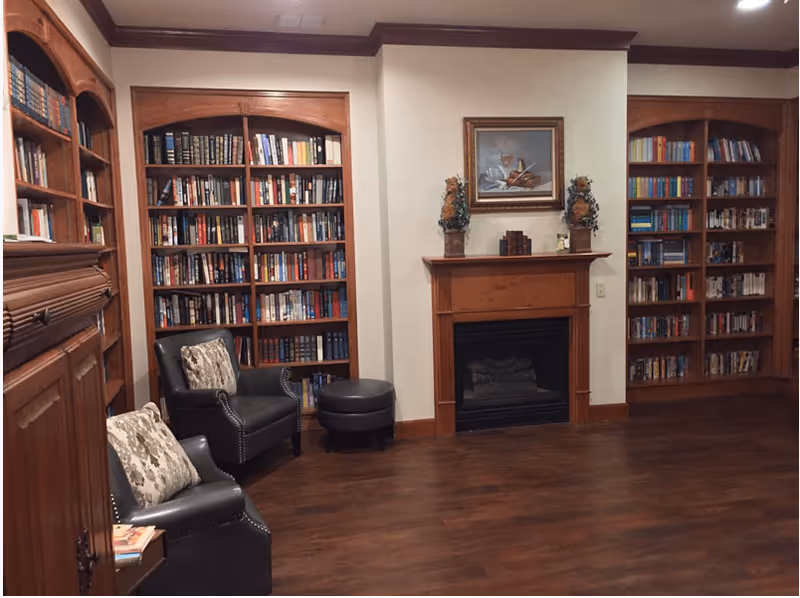 Cozy library-style living room with built-in bookshelves, a fireplace, and leather armchairs.