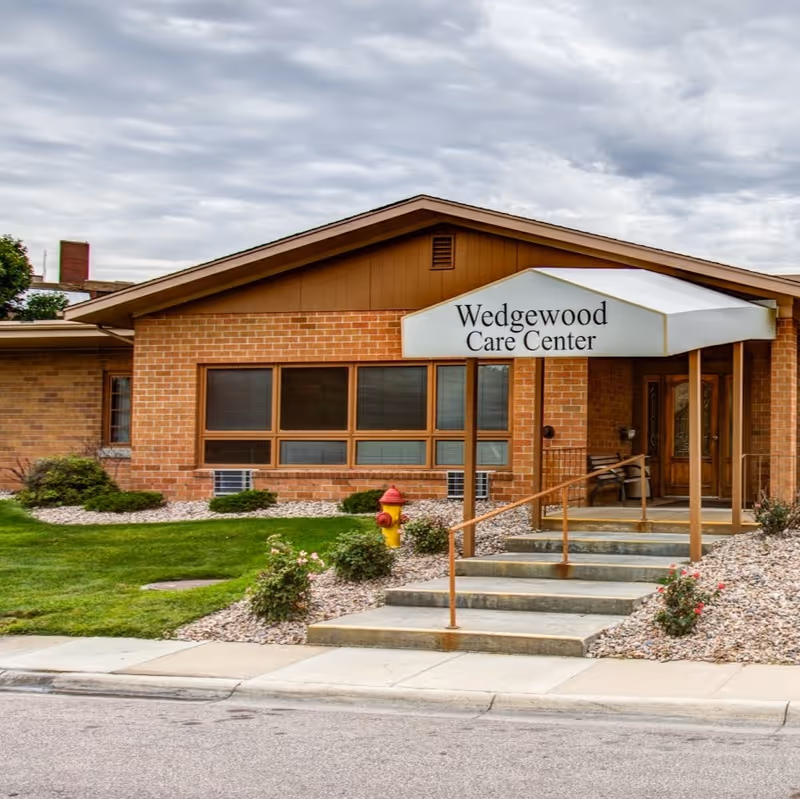 Front entrance of Wedgewood Care Center with a brick facade, covered awning, steps, and landscaped walkway.