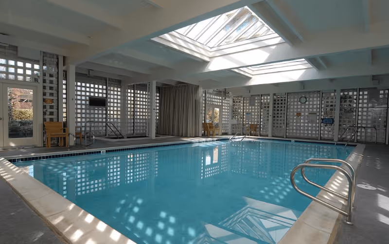 Indoor swimming pool room with skylights, metal handrails, lounge chairs, and lattice-patterned walls.