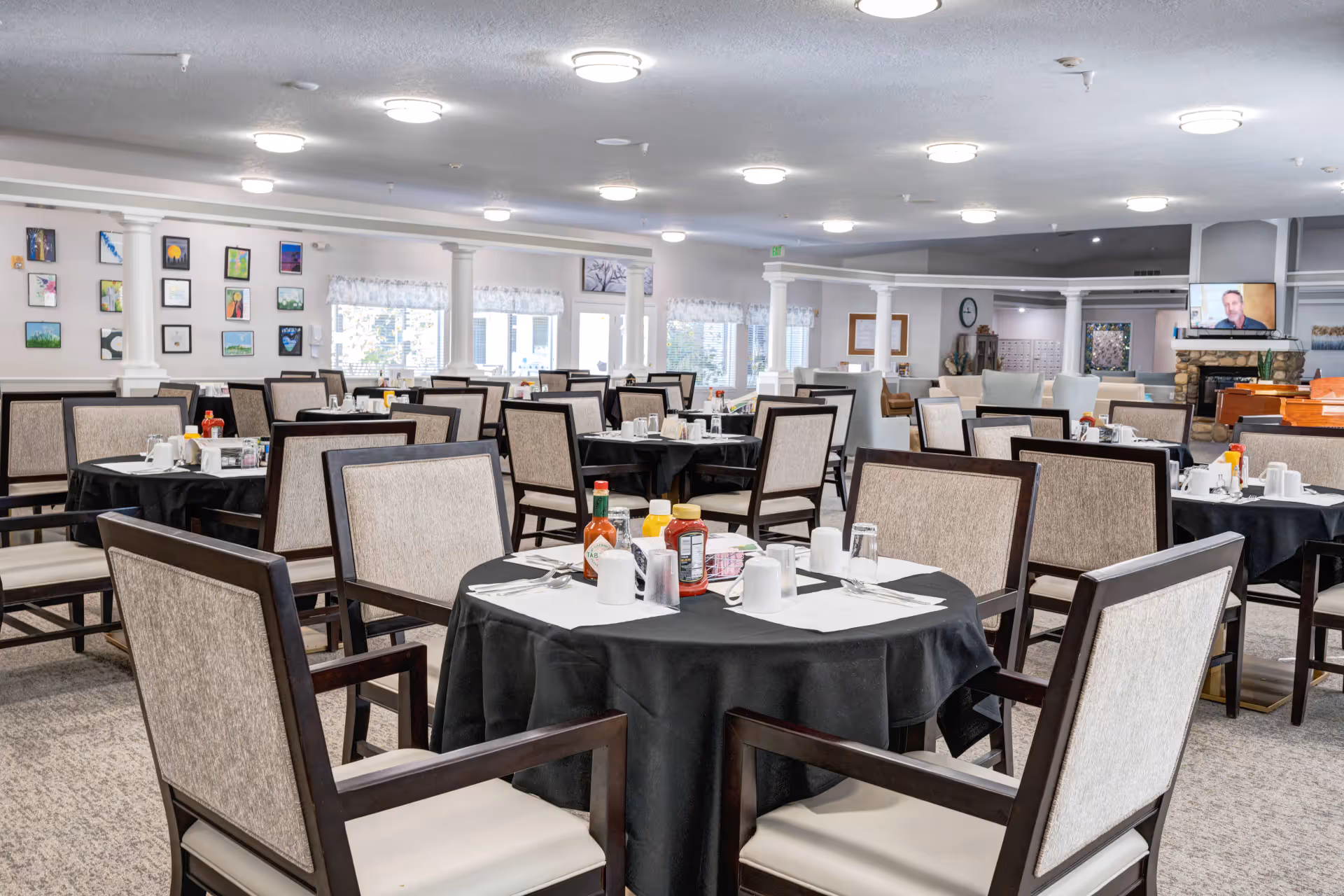 Spacious dining room with round tables covered in black tablecloths and chairs set for meals.