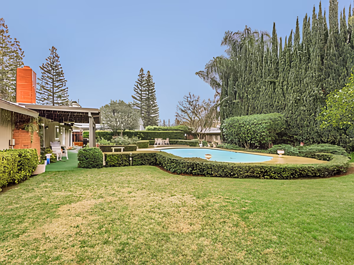 Well-maintained outdoor courtyard with a circular swimming pool surrounded by hedges, lawn, and an adjacent building.
