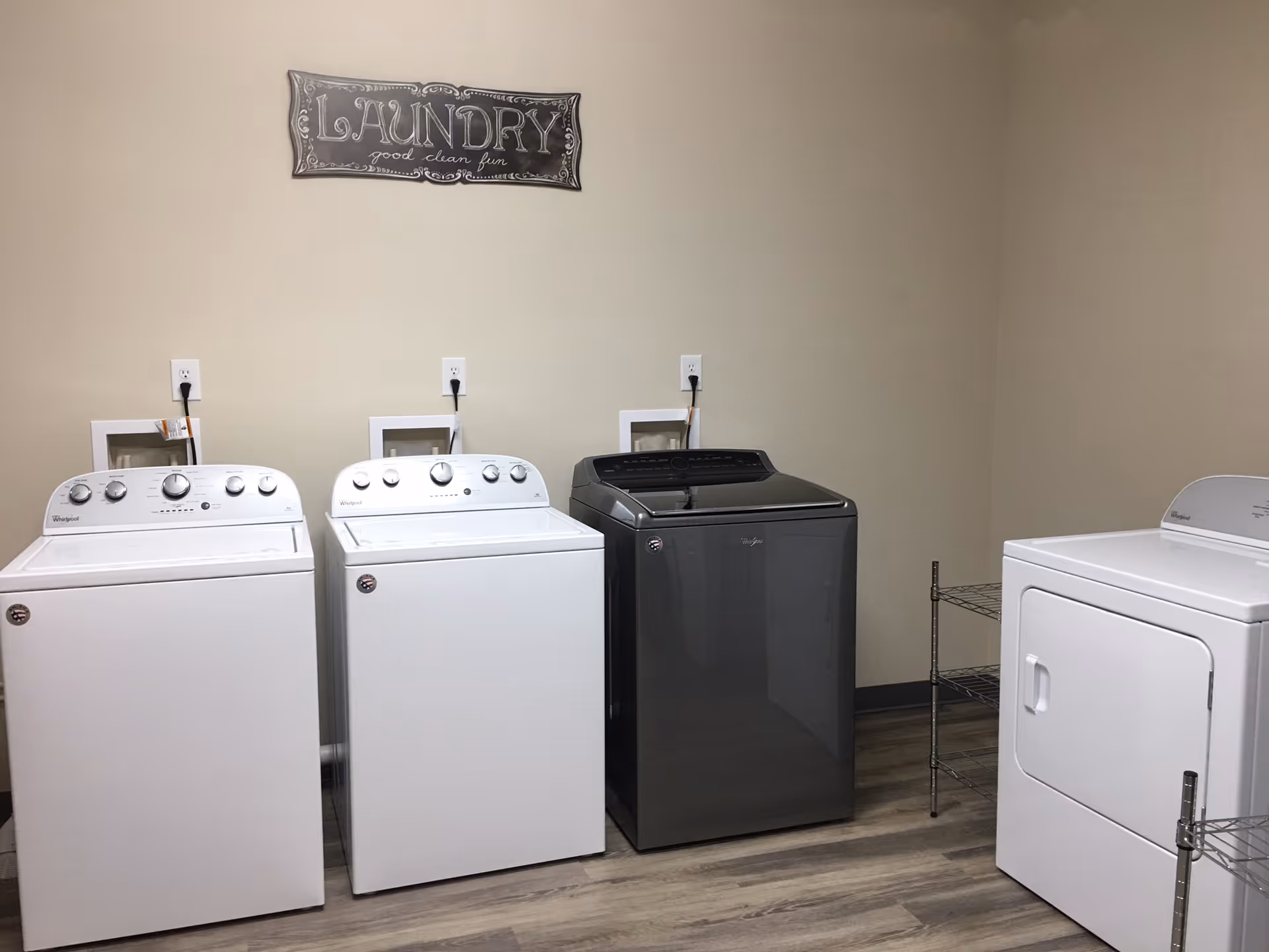 Laundry room with three washing machines and a dryer along a beige wall beneath a decorative 'LAUNDRY' sign.