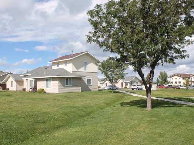 Rendezvous Apartments exterior with beige buildings, green lawns, and a large tree.