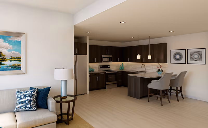 Open-concept living area with a beige sofa and side table in the foreground and a modern kitchen with dark wood cabinets and an island with bar stools.